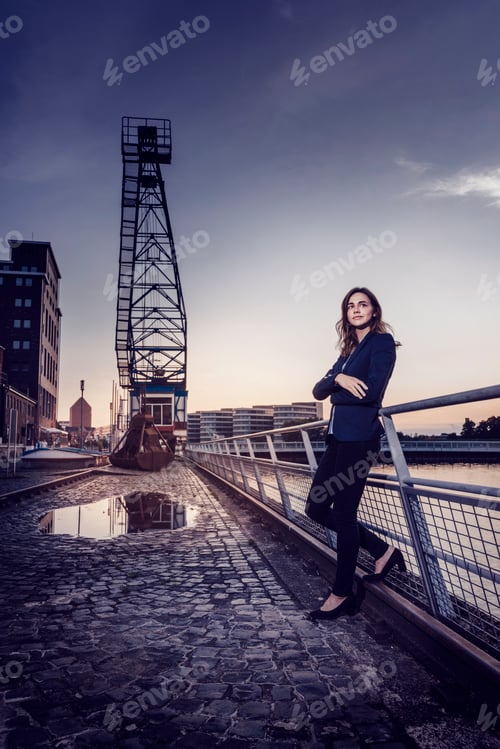 Preview: Businesswoman standing at wet inner harbor, thinking