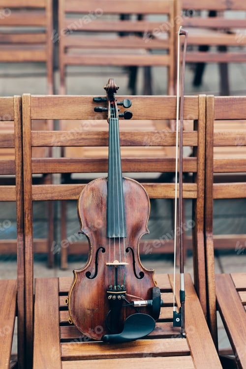 Preview: Vertical shot of violin with bow on wooden chair. String musical instrument prepared for concert