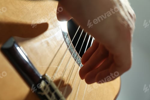 Preview: Man playing on classic guitar against light background, closeup