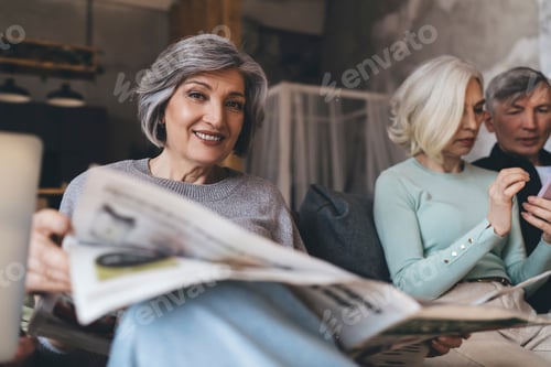 Preview: Smiling senior woman with newspaper relaxing on sofa with friends