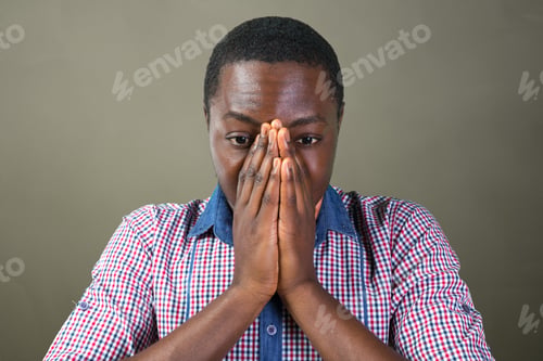 Preview: Man covers face with hands expressing concern in front of gray background