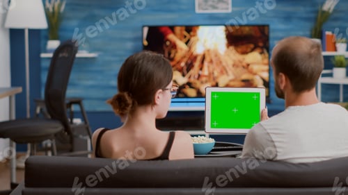 Preview: Couple relaxing on sofa looking at social media video content using digital tablet with green screen