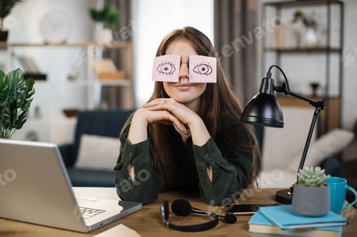 Preview: Tired caucasian female student sleeping with stickers on eyes, sitting at table