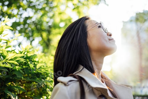 Preview: A young Korean woman in a coat stands in a city park and looks up