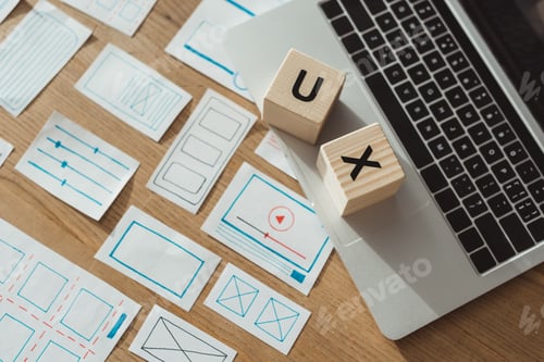 Preview: High angle view of cubes with ux letters on laptop with website wireframe sketches on wooden table
