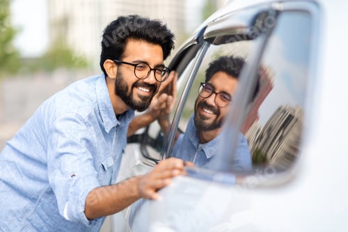 Preview: Smiling eastern guy looking at beautiful white auto in showroom