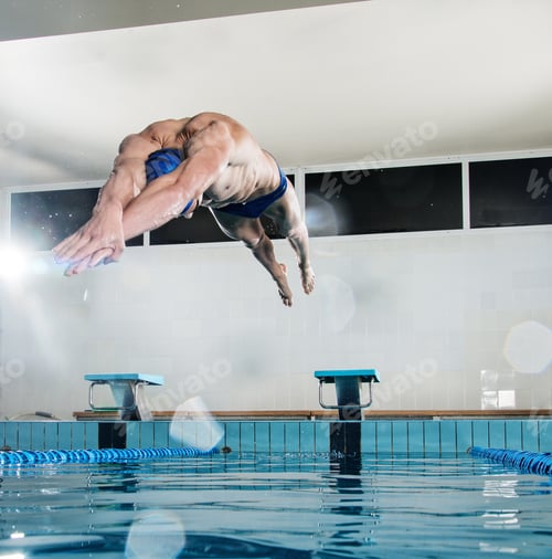 Preview: Young muscular swimmer jumping from starting block in a swimming pool