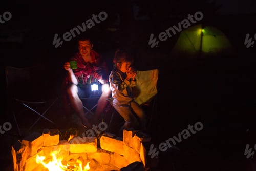 Preview: Dad and daughter sit at night by the fire in the open air in the summer in nature