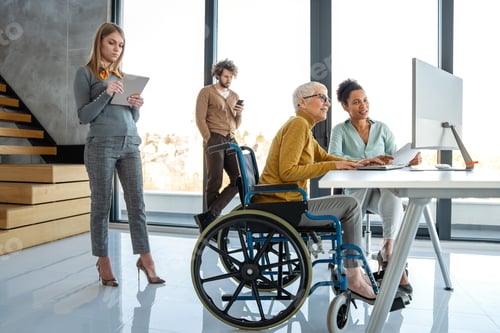 Preview: Disabled woman in wheelchair looking at computer, discussing startup project with interracial team