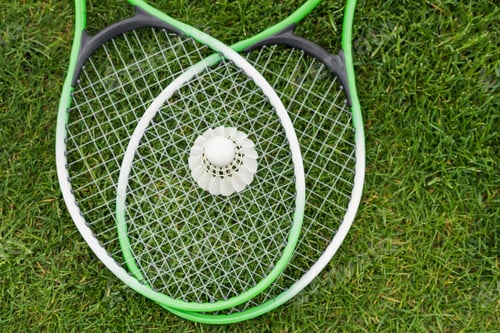 Preview: top view of shuttlecock on badminton rackets lying on green grass
