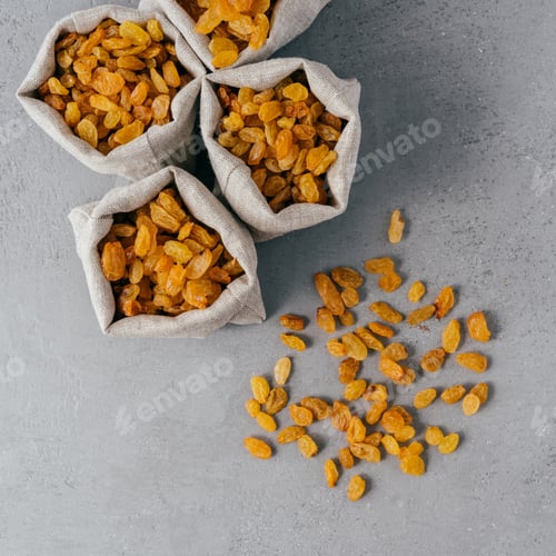 Preview: Golden raisins from dried grapes in burlap textile sacks photographed from above.
