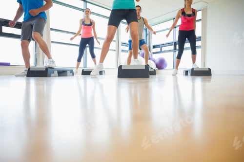 Preview: Low Section Of Instructor With Fitness Class Performing Step Aerobics Exercise In Gym
