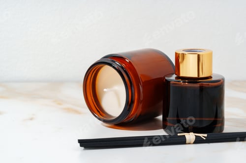 Preview: Brown Glass Candle and Diffuser Bottles on Marble Surface With Dried Branches