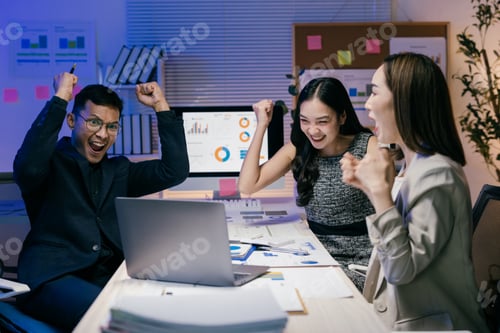 Preview: Group of asian businesspeople raising arms and cheering while working late in the office, celebratin
