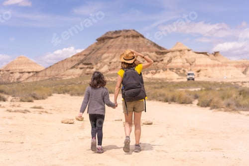 Preview: Rear view of mother and daughter walking along a desert