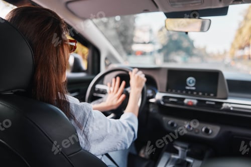 Preview: A woman sits in the driver's seat of a car, gripping the steering wheel with one hand, focused on