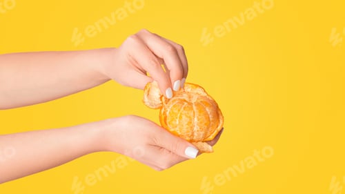 Preview: Millennial girl peeling fresh orange fruit on pink background, close up of hands