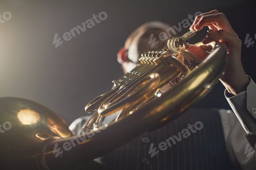 Preview: Male Musician Playing French Horn on Stage Pushing Valve Levers under Spotlight