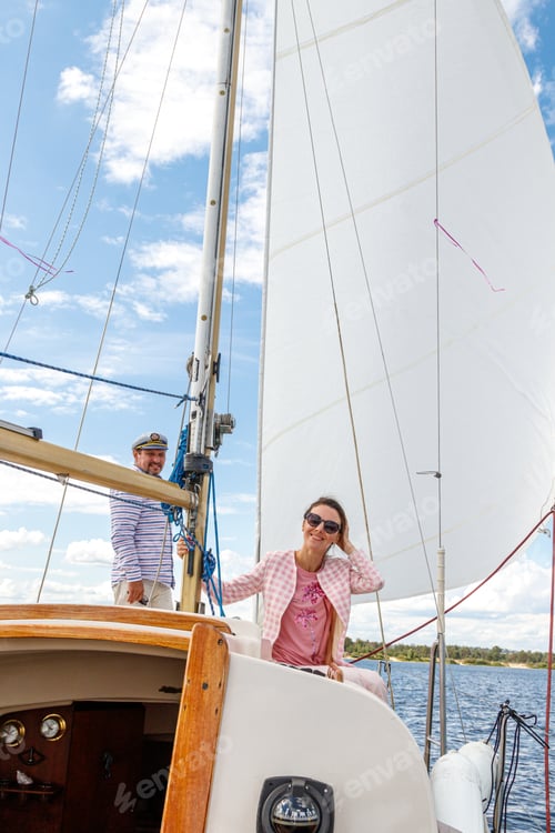 Preview: sailor man in a cap with a girl on a boat under sail against the sky and water