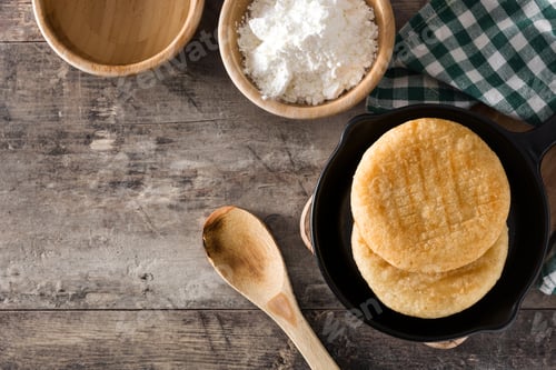 Preview: Delicious arepas in frying pan with precooked corn flour on rustic wooden table