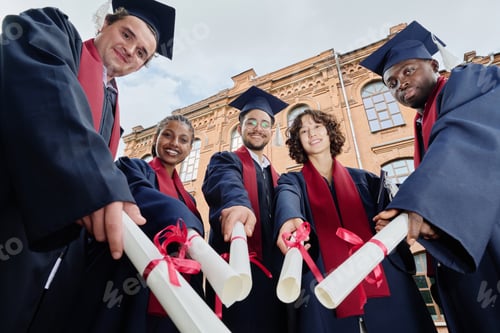 Preview: Graduated students with diplomas standing outdoors