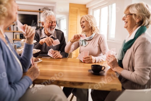 Preview: Cheerful senior friends having fun while playing cards together.