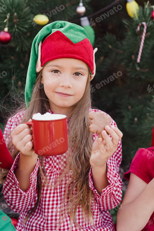 Preview: Merry Christmas. Portrait of two funny children girls in Santa hat eating gingerbread cookies