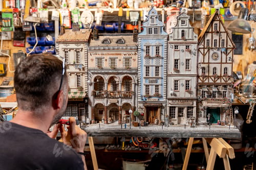 Preview: Modeller man working at scale model of miniature building in his workshop full of tools