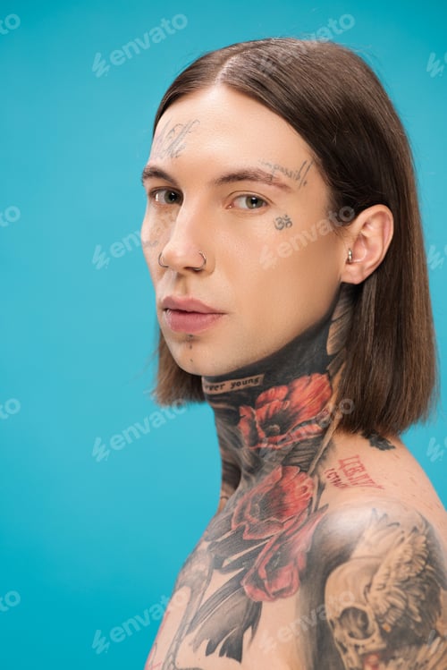 Preview: young and pierced man with tattoos looking at camera isolated on blue