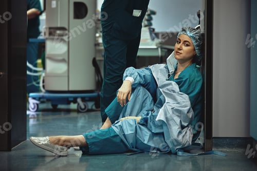 Preview: Tired doctor sitting after surgery in the hospital corridor. Great burden on doctors and medicine