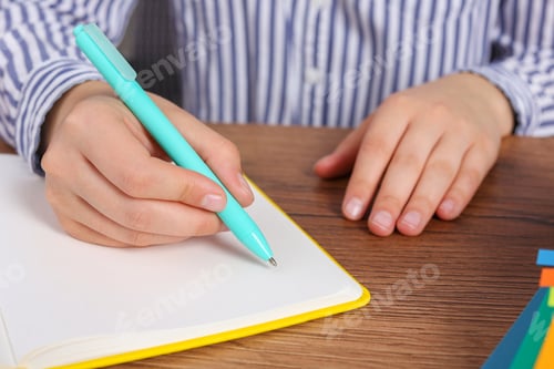 Preview: Woman writing in notebook at wooden table, closeup