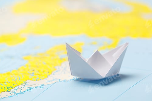 Preview: Paper boat floats on a map showing coastlines and land features