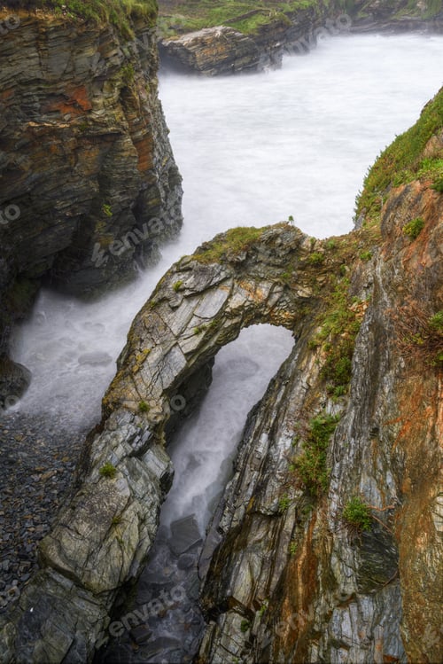 Preview: The waves reach the stony shore and the arch