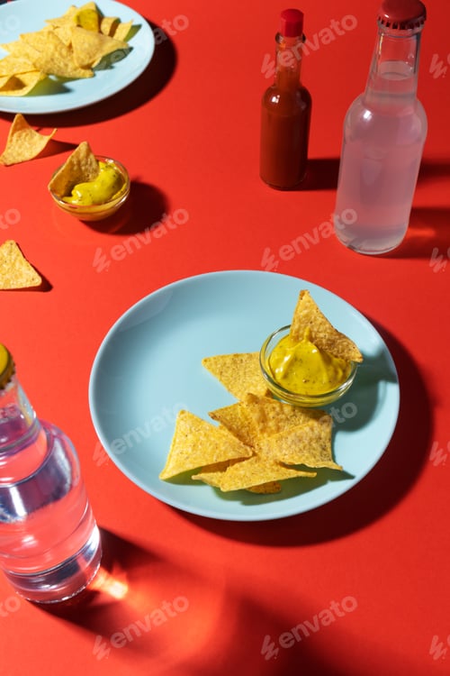 Preview: Nachos chips with cheese sauce on blue plate, soda bottle and hot sauce on red backgro