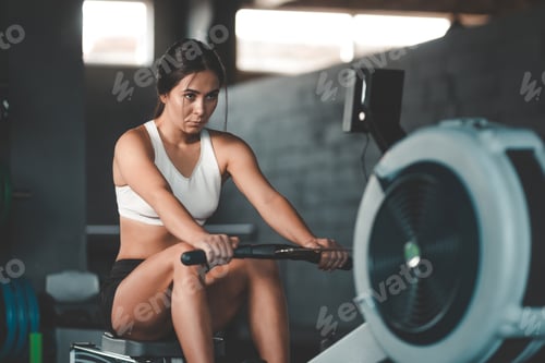 Preview: Concentrated athletic girl doing exercise on the rowing machine