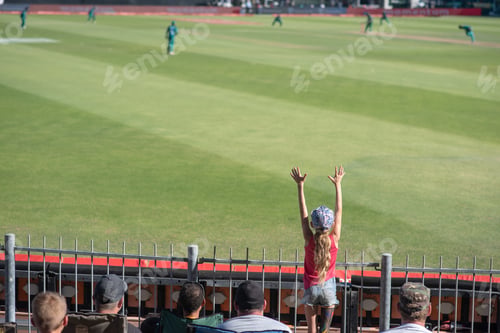 Preview: Young fan throwing up her hands in excitement at cricket game.