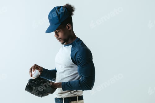Preview: handsome african american sportsman in baseball glove holding ball isolated on grey