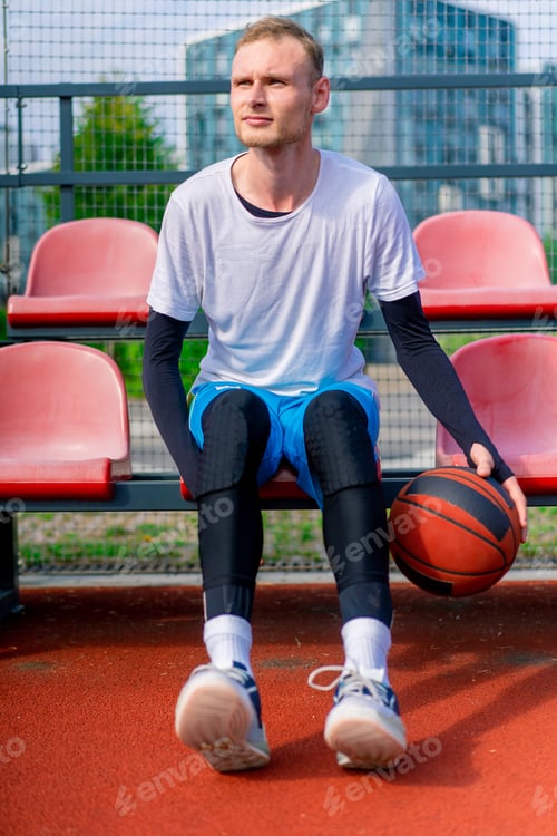 Preview: A tall guy basketball player sits in the bleachers of an outdoor basketball court