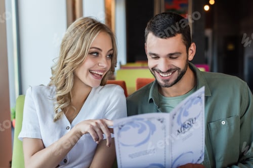 Preview: cheerful woman pointing with finger near smiling boyfriend choosing meal from menu