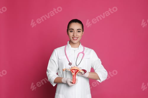 Preview: Doctor demonstrating model of female reproductive system on pink background. Gynecological care