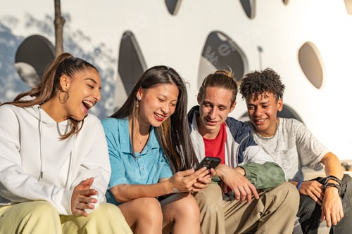 Preview: Group of happy teenage friends looking the phone and laughing in the city street.