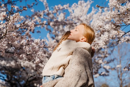 Visualização: Mãe e filha felizes juntas no jardim de árvores florescentes na primavera sob a luz do sol.