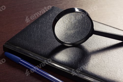 Preview: Notebook and magnifying glass on wooden table with pen nearby at desk location