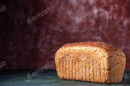 Preview: Close up view of packed black bread on the left side on maroon distressed background with free space