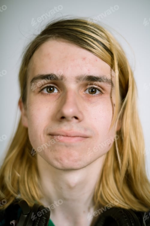 Preview: Portrait of a real young man on a light background in a plaid shirt with headphones around his neck.