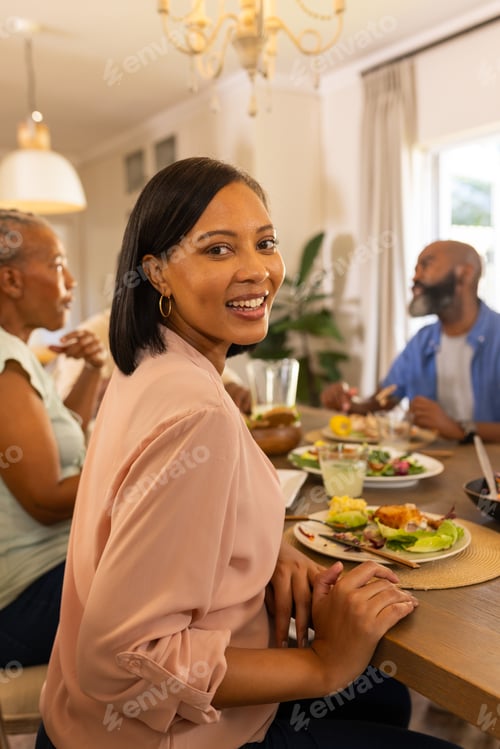 Preview: Smiling woman enjoying meal with family at dining table, sharing quality time
