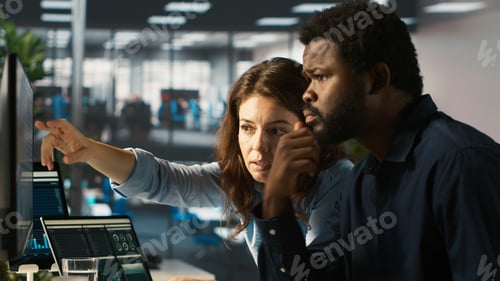 Preview: Employee and coworker looking over revenue figures on PC in office