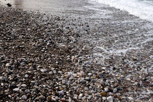 Preview: A beach with small and large multicolored pebbles with a foam trail