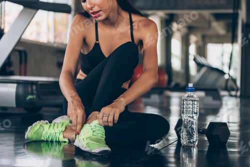 Preview: Young active Caucasian sporty woman tying shoelace on green shoes in gym