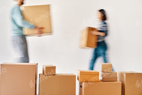 Preview: Blurred motion of young couple carrying cardboard boxes moving to new house